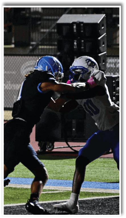 A person wearing a blue helmet and black sports uniform with pink socks is running on a football field while holding a football. Description generated by AI