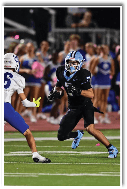 Two people in football uniforms are on a field with one person running with the ball and the other preparing to defend. Description generated by AI