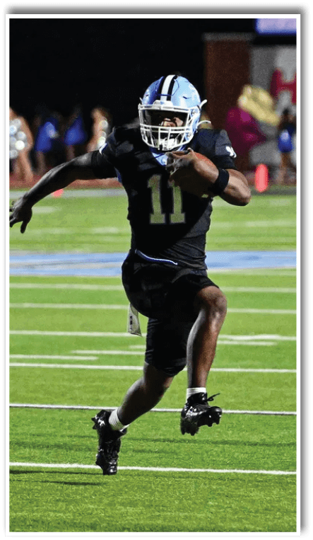 A person in athletic gear is running on a football field with a blurred background showing cheerleaders and a sign that reads “HOOVER." Description generated by AI