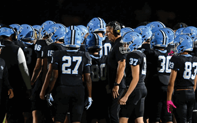 A group of people wearing blue helmets and black sports uniforms are gathered closely together, with one person wearing a headset appearing to give instructions. Description generated by AI