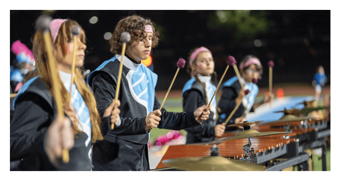 People wearing matching uniforms and headbands are playing mallet percussion instruments outdoors at night. Description generated by AI