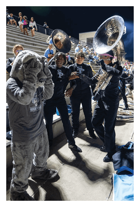 People in a marching band uniform and sequined dance costumes perform on a football field at night. Description generated by AI