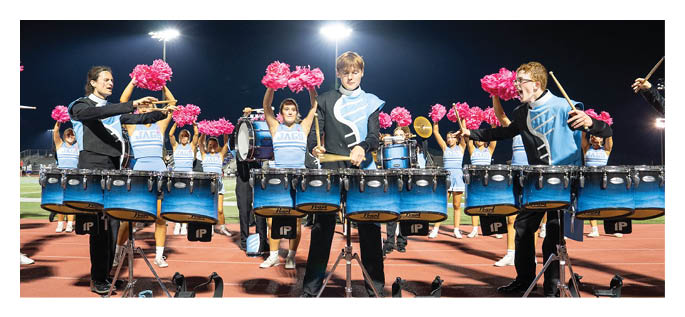 People in matching uniforms perform with drums and pink pom-poms on a lit outdoor track at night. Description generated by AI