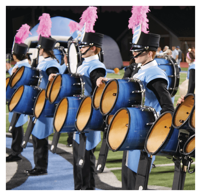 Adults in matching uniforms and hats stand in a line playing blue marching band drums on a field. Description generated by AI