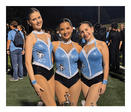 Three people wearing matching performance outfits and white boots stand behind three trophies on a sports field. Description generated by AI