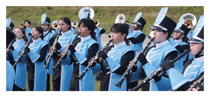A group of people dressed in blue and black marching band uniforms are standing outdoors playing clarinets. Description generated by AI