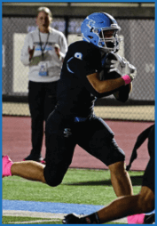 A person wearing black athletic clothing and bright pink socks is running or jumping on a sports field with a blue and white line. Description generated by AI