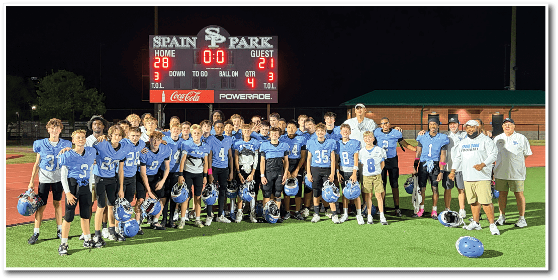 A group of people in blue sports uniforms and helmets pose together on a football field in front of a scoreboard showing the final score. Description generated by AI