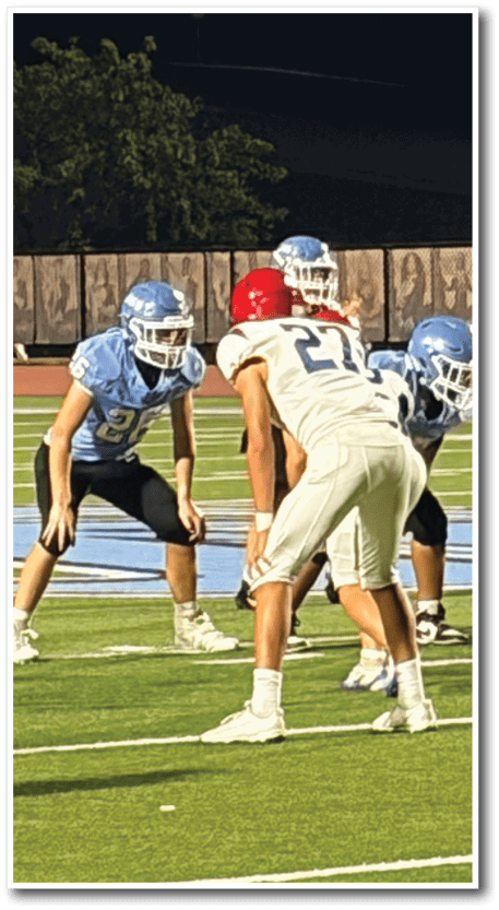 People in football uniforms are positioned on a field, appearing to prepare for a play during a game. Description generated by AI