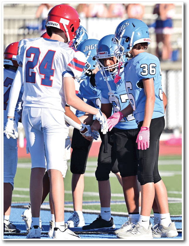 Children wearing football helmets and uniforms are gathered closely together, appearing to be in a huddle during a game or practice. Description generated by AI