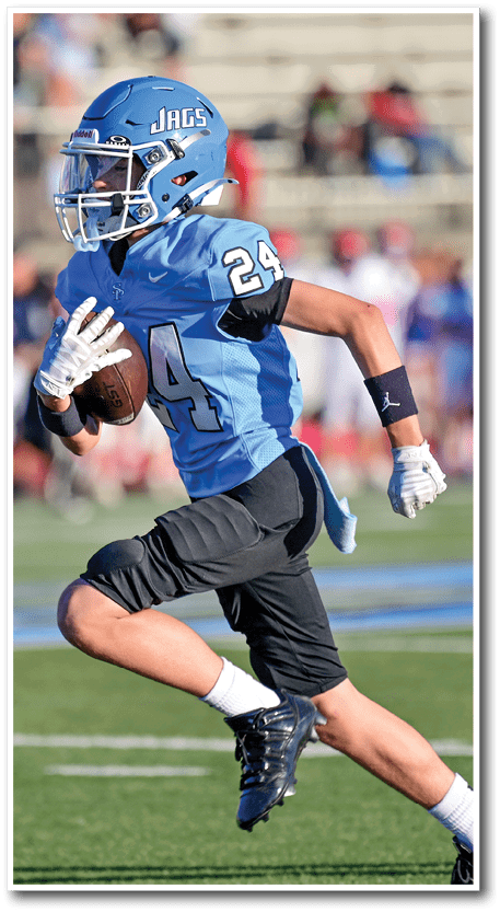 A person wearing a blue football uniform with the number 24 and a helmet labeled JAGS is running on a football field while holding a football. Description generated by AI