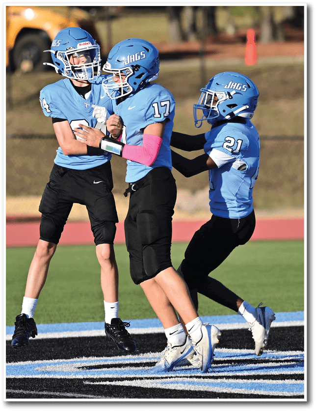 Two people in blue football uniforms with helmets are standing on a field, with one person placing a hand on the other's shoulder. Description generated by AI