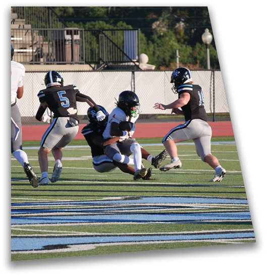 Several people in football uniforms are on a field with one person tackling another who is holding a football. Description generated by AI