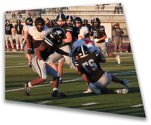 Two people in black football uniforms are tackling a person in a white and red football uniform on a grassy field during a game. Description generated by AI