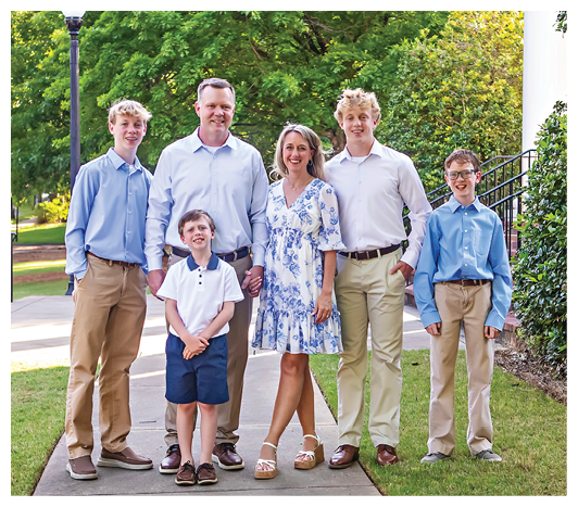 Five people stand on grass and dirt with only their legs and feet visible, wearing casual pants, shorts, and sandals or shoes. Description generated by AI