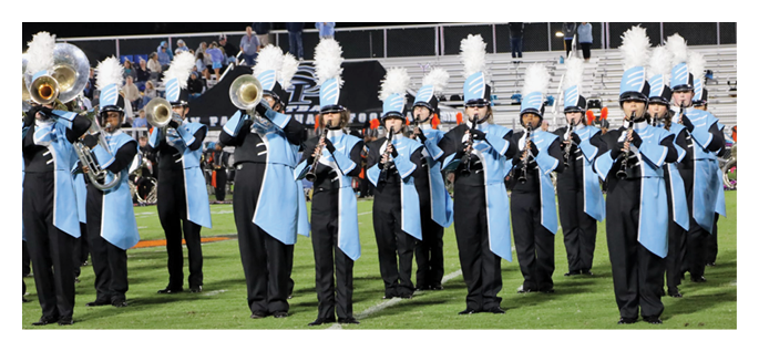A marching band dressed in blue and black uniforms with white plumed hats is performing on a football field. Description generated by AI
