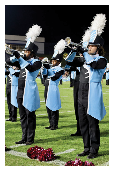 People in blue and black marching band uniforms with tall white plumes on their hats are playing trumpets on a grassy field. Description generated by AI