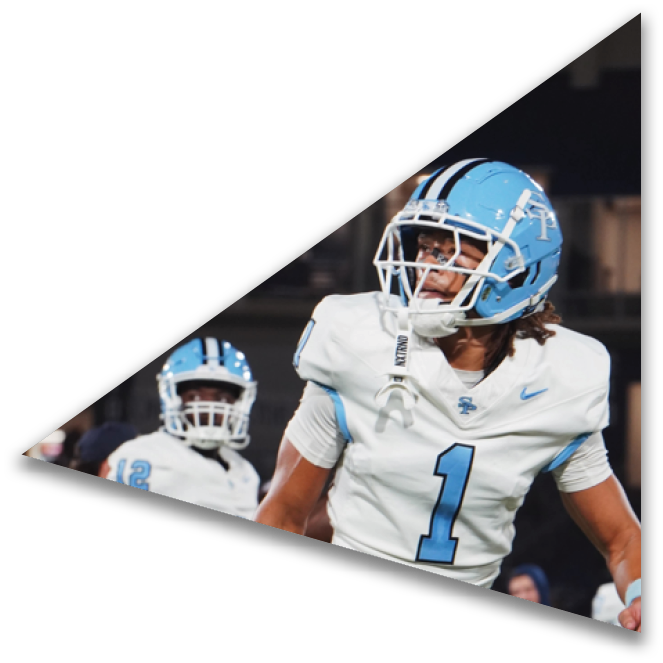 Two people in white and light blue football uniforms are on a field, with one person wearing a helmet and the number one on their jersey. Description generated by AI