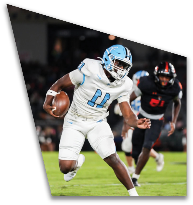 A person wearing a light blue helmet and white football uniform is holding a football and appears to be running during a game. Description generated by AI