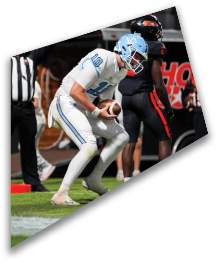 A person in white athletic gear is holding a football and preparing to make a play on a grassy field with other people standing nearby. Description generated by AI