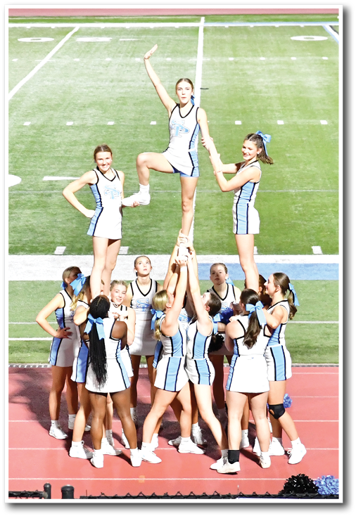 A group of people in matching cheerleading uniforms perform a stunt on a track field with one person elevated above the others holding a pose. Description generated by AI