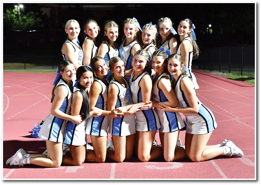 A group of people wearing matching cheerleading uniforms are kneeling and posing together on a track at night. Description generated by AI