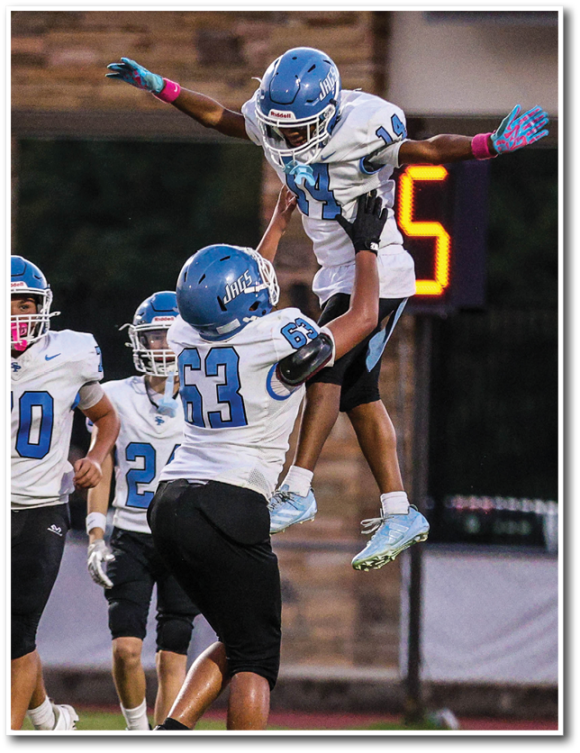 Two people in football uniforms celebrate with one person lifting the other in the air on a sports field. Description generated by AI