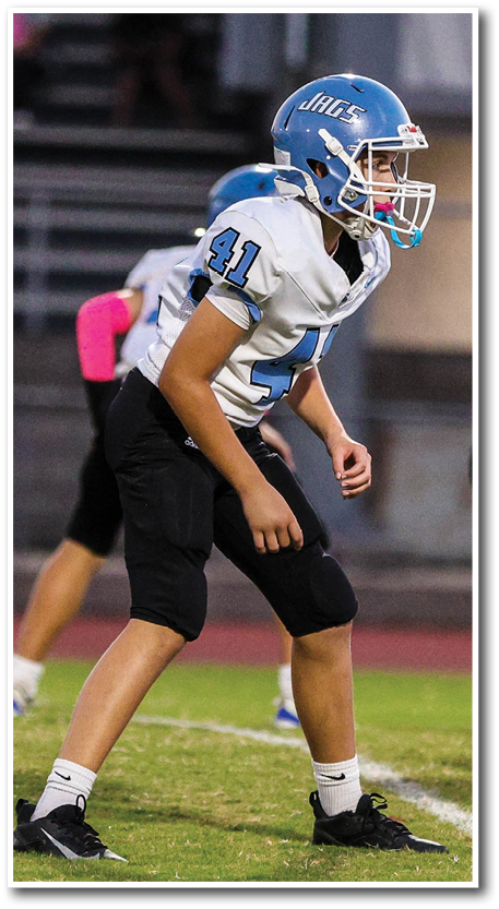 A person wearing a blue helmet and white football jersey with the number 41 is preparing to play on a football field. Description generated by AI