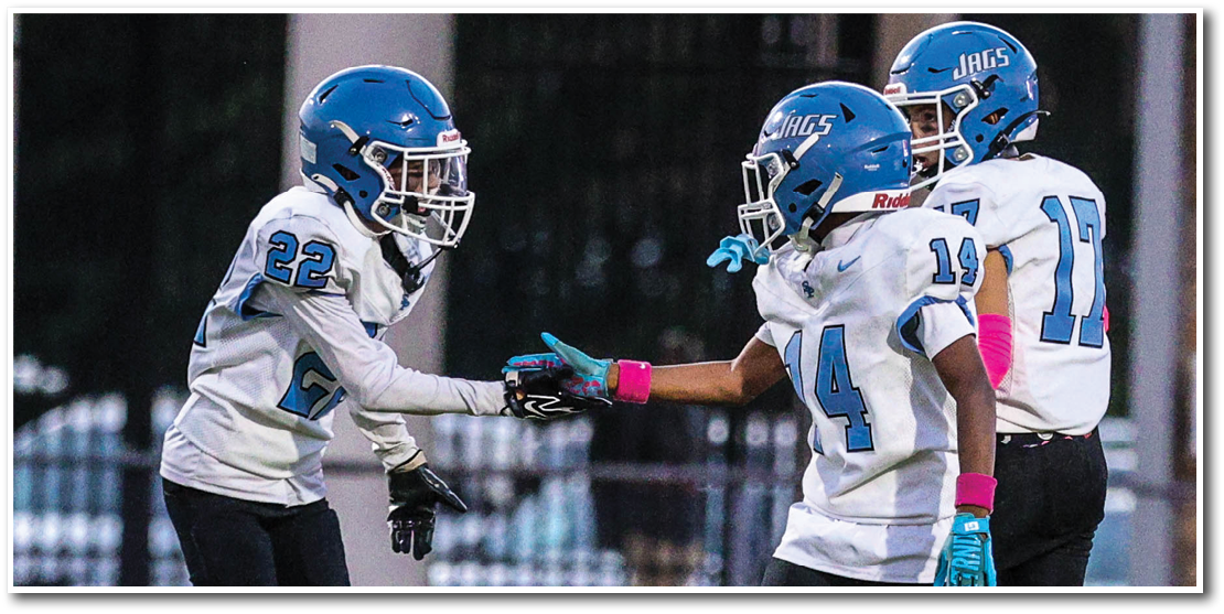Three people wearing blue helmets and white football uniforms are on a field with two of them fist bumping. Description generated by AI
