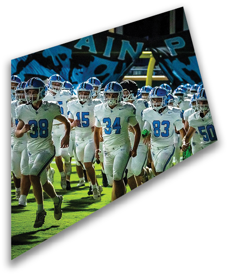A group of people wearing white football uniforms with blue helmets are running onto a green field under stadium lights. Description generated by AI