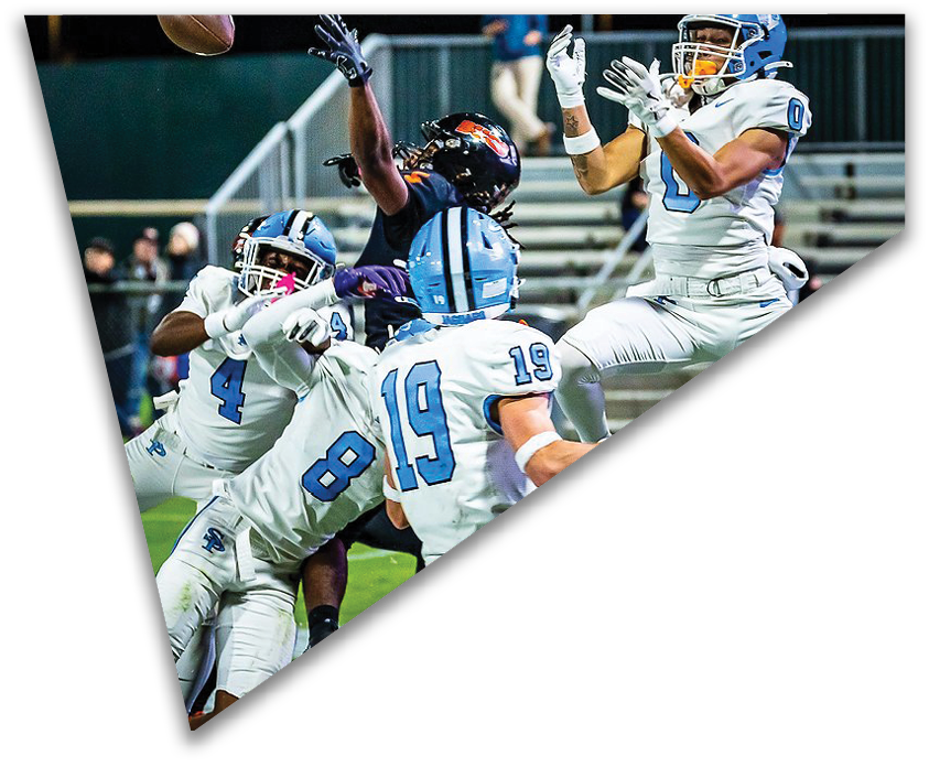 Several athletes in football uniforms are actively engaged in a play on a field with empty bleachers in the background. Description generated by AI