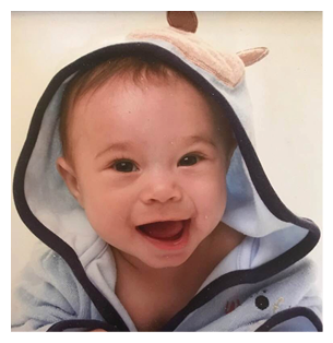 A baby wearing a blue and white hoodie is smiling and sitting on a bed. AI generated content