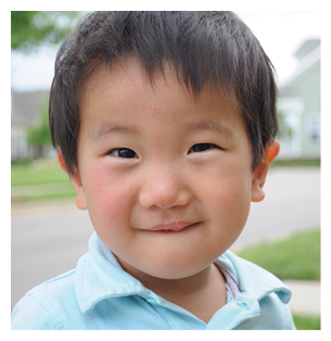 A young boy with a blue shirt and white collar is standing on the sidewalk. AI generated content