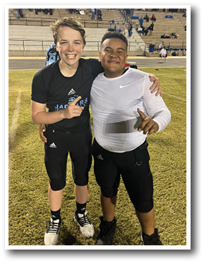 Two young men are standing on a field, posing for a picture. One of them is wearing a black shirt and the other is wearing a white shirt. They are both holding their hands on their shoulders. AI generated content