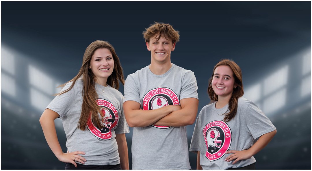 Three smiling adults wearing matching gray t-shirts with a sports logo and black shorts or skirts stand confidently on a football field under stadium lights. Description generated by AI