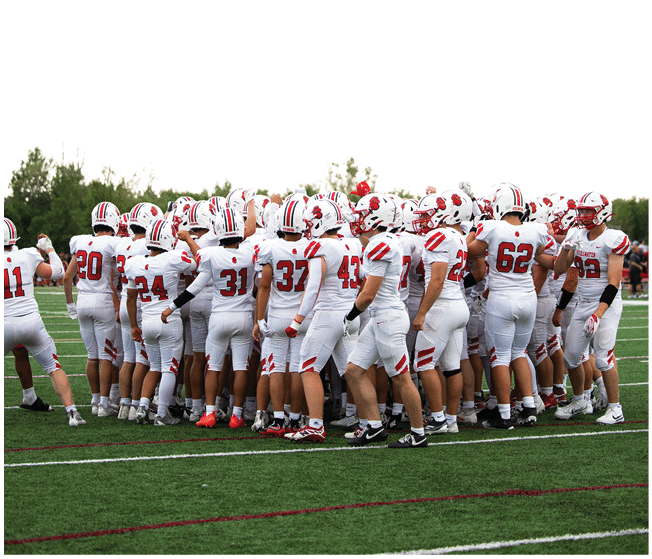 A group of people wearing white football uniforms with red and black accents are gathered closely together on a green field, appearing to be in a team huddle. Description generated by AI