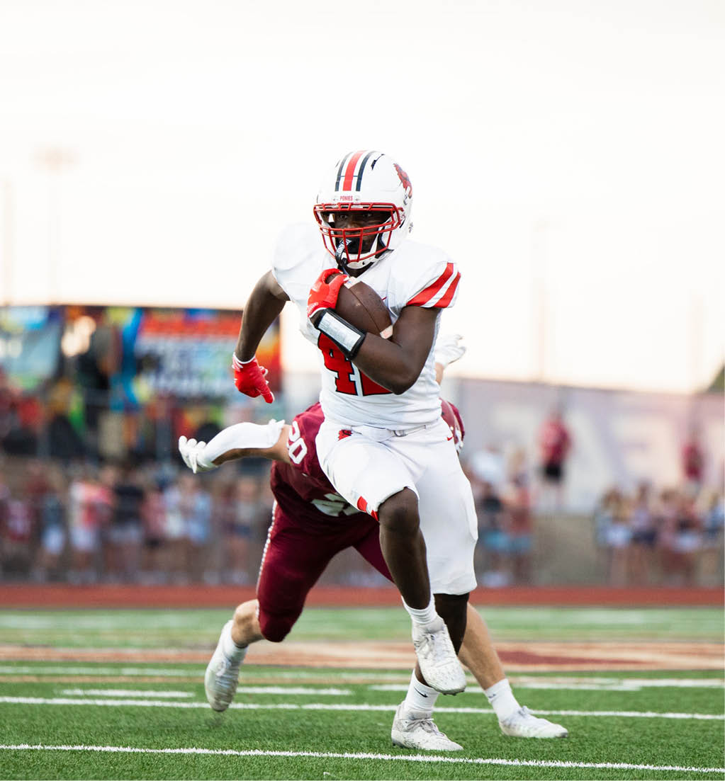 A person in white football gear is running with the ball while another person in maroon gear attempts to tackle them on a football field. Description generated by AI