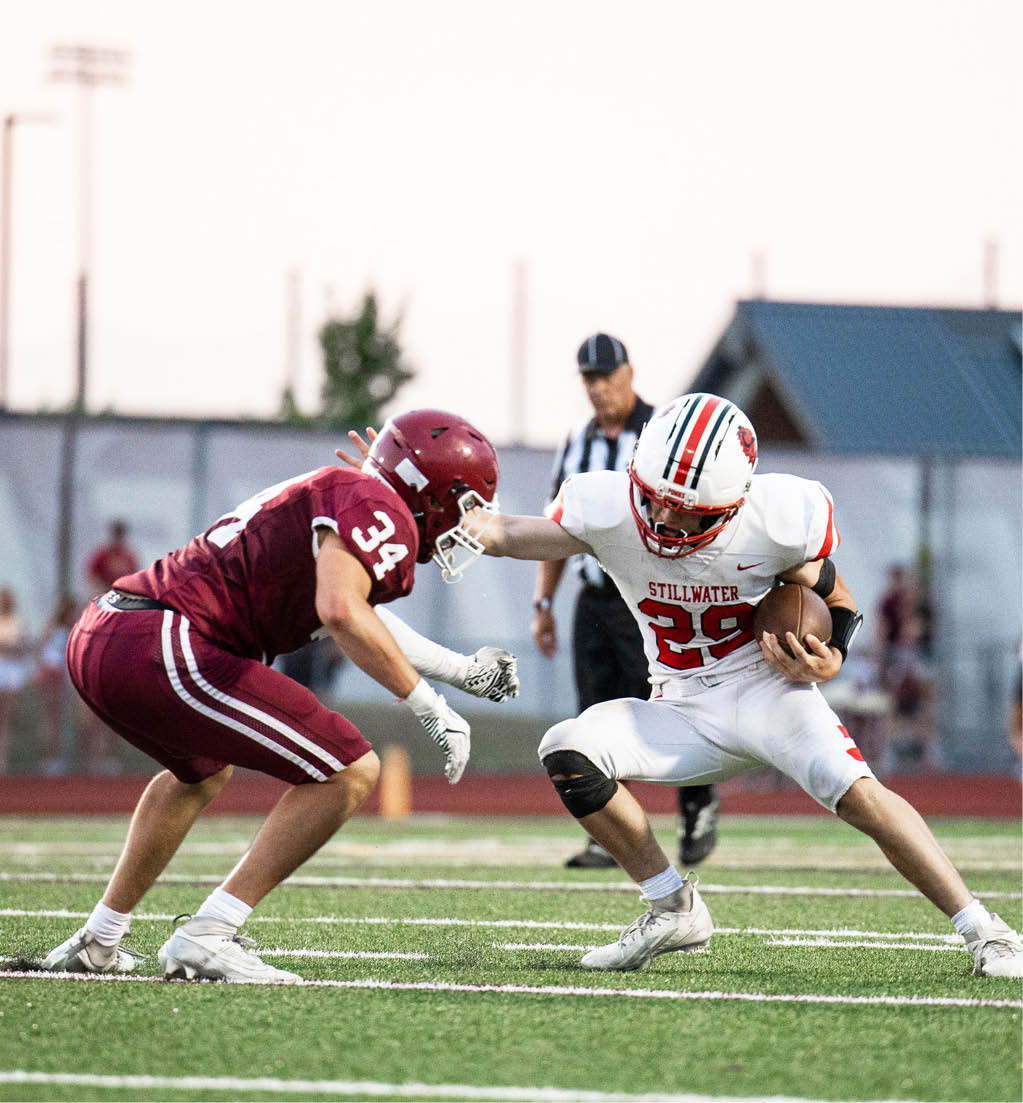 Two people in football uniforms are engaged in a play on a field with one person in a maroon uniform crouching and the other in a white uniform holding a football. Description generated by AI