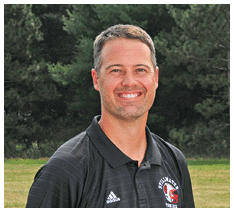 A person with short hair wearing a black Adidas polo shirt with a logo stands smiling outdoors in front of trees and grass. Description generated by AI