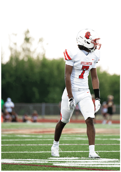 A group of people wearing white football uniforms with red and black accents are sitting and standing closely together on a sports field. Description generated by AI