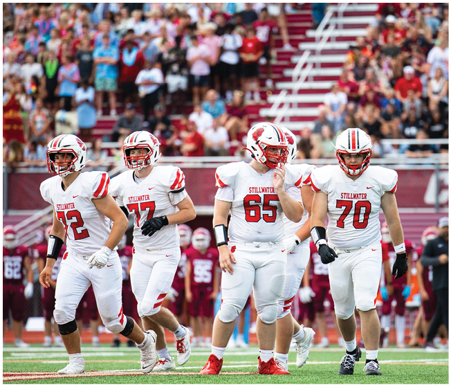 A group of people wearing white football uniforms with red and black accents are sitting and standing closely together on a sports field. Description generated by AI