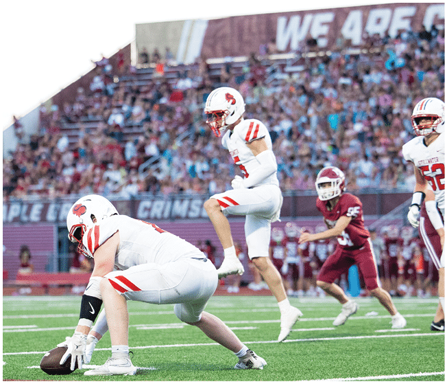 A group of people wearing white football uniforms with red and black accents are sitting and standing closely together on a sports field. Description generated by AI