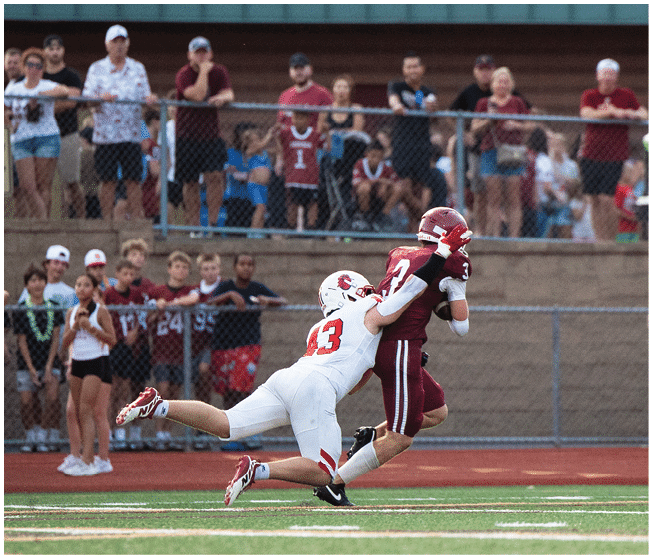 A group of people wearing white football uniforms with red and black accents are sitting and standing closely together on a sports field. Description generated by AI