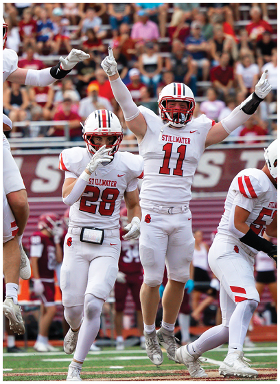 A person in a white football uniform with red accents is holding a football and appears to be running during a game. Description generated by AI