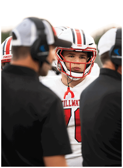 A person in a white football uniform with red accents is holding a football and appears to be running during a game. Description generated by AI