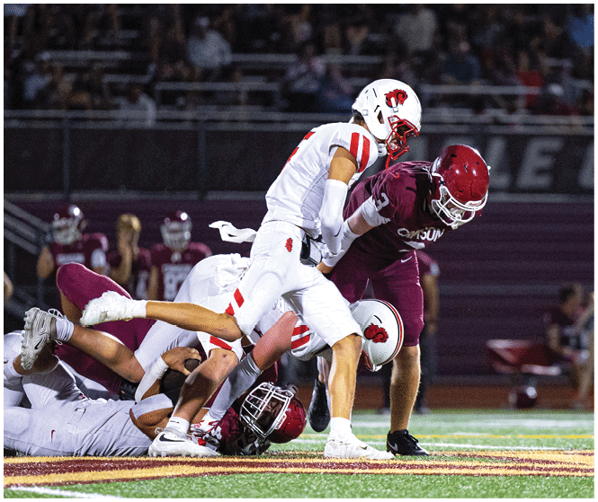 A person in a white football uniform with red accents is holding a football and appears to be running during a game. Description generated by AI