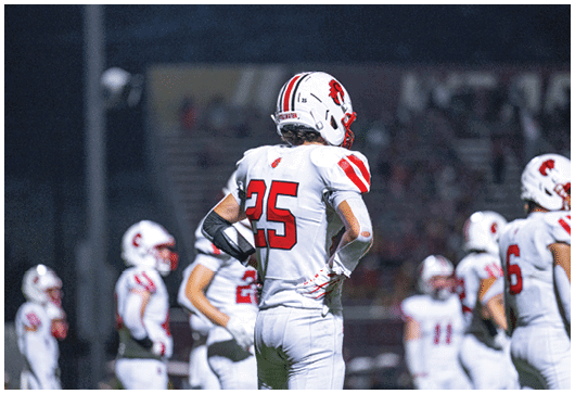 A person in a white football uniform with red accents is holding a football and appears to be running during a game. Description generated by AI
