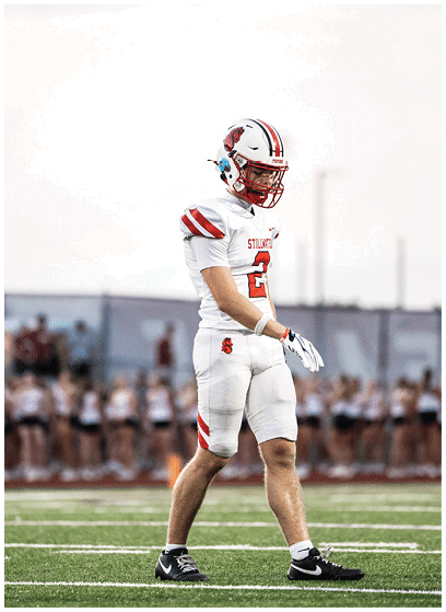 A person in a white football uniform with red accents is holding a football and appears to be running during a game. Description generated by AI