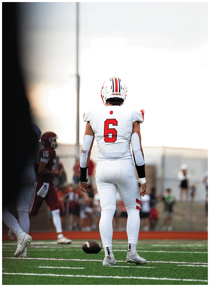 A person in a white football uniform with red accents is holding a football and appears to be running during a game. Description generated by AI