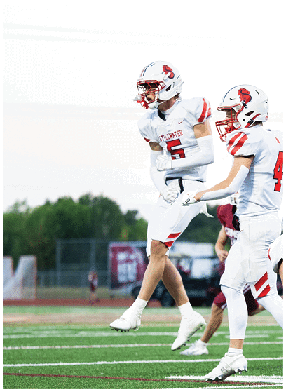 A person in a white football uniform with red accents is holding a football and appears to be running during a game. Description generated by AI